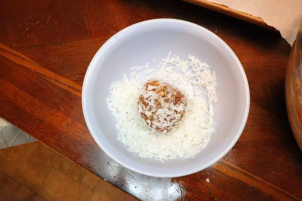 rolling a chocolate coconut energy ball into shredded coconut