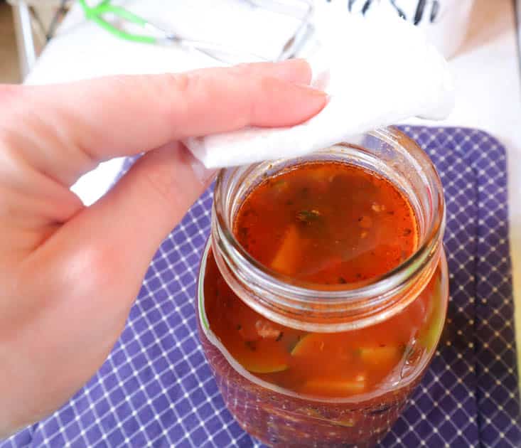 hand wiping rim of mason jar removing spilled soup